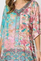 Woman wearing a colourful pink and blue printed floaty top with elbow length sleeves and detailed border and neckline.