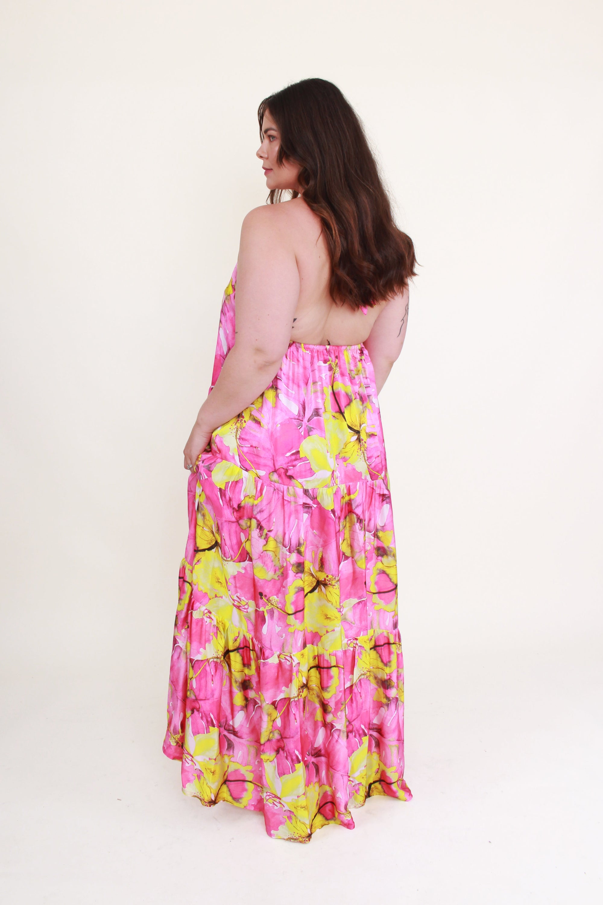 Woman wearing a pink and yellow floral dress on a white background back