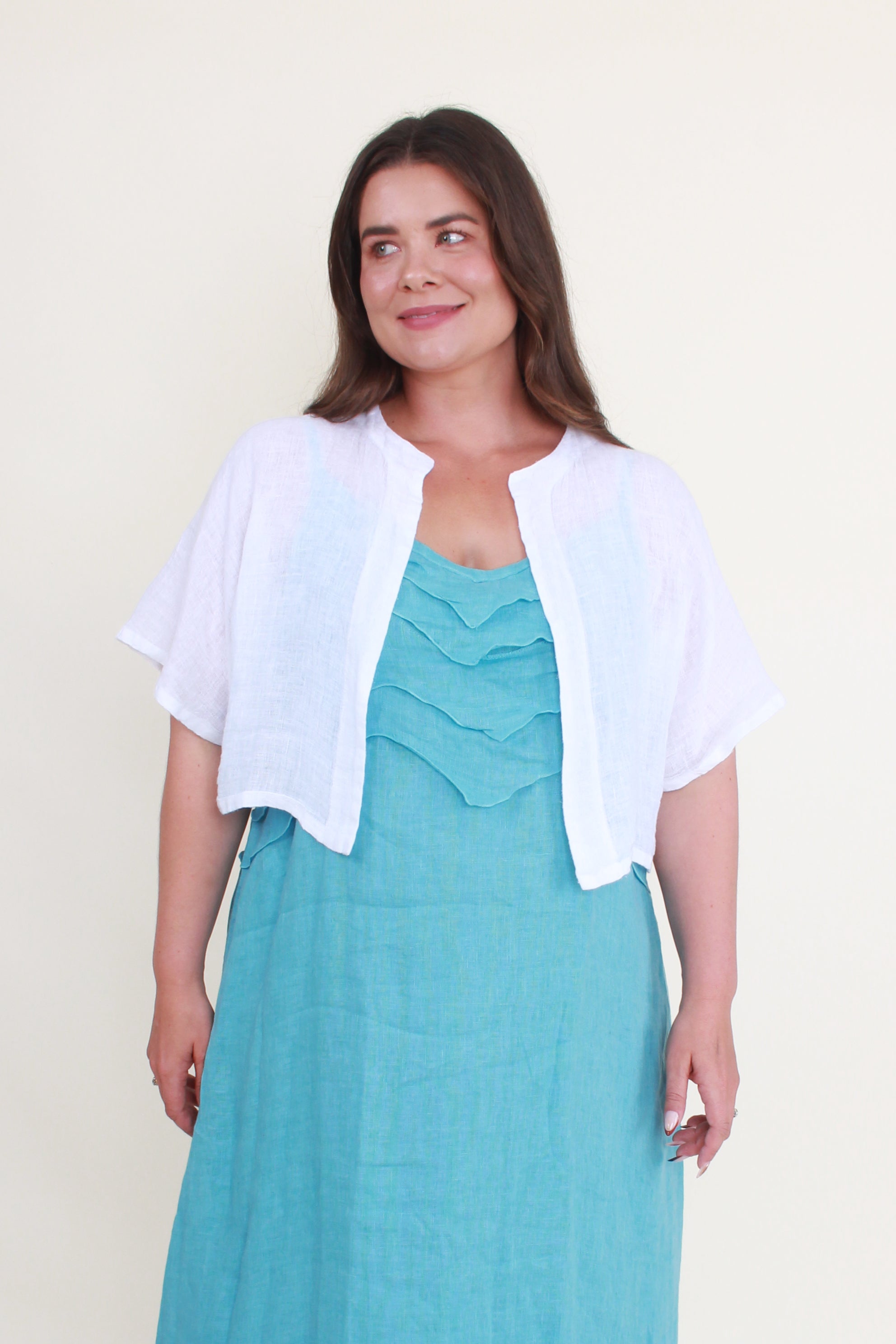 Woman wearing a teal dress with a white cardigan against a light background