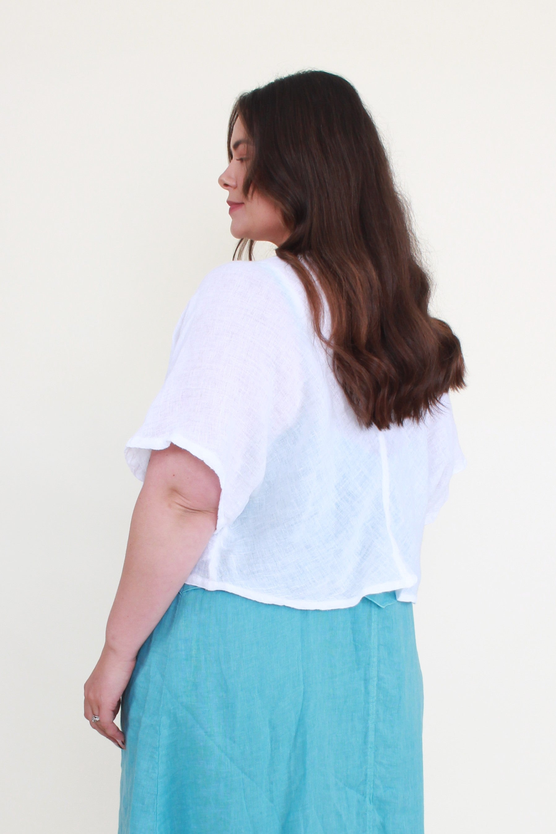 Woman wearing a white top and teal pants against a plain background