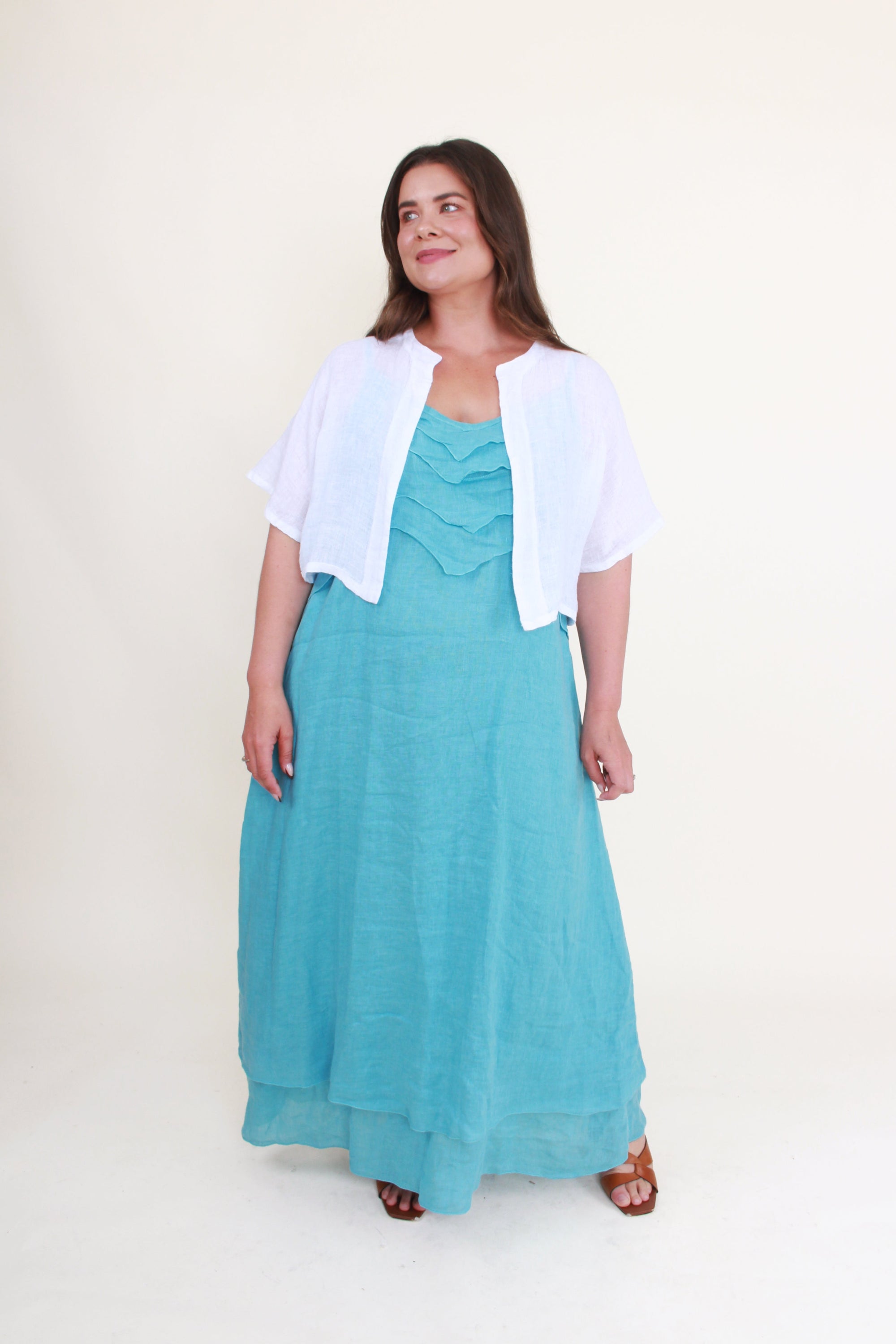 Woman wearing a turquoise dress with a white cardigan on a white background