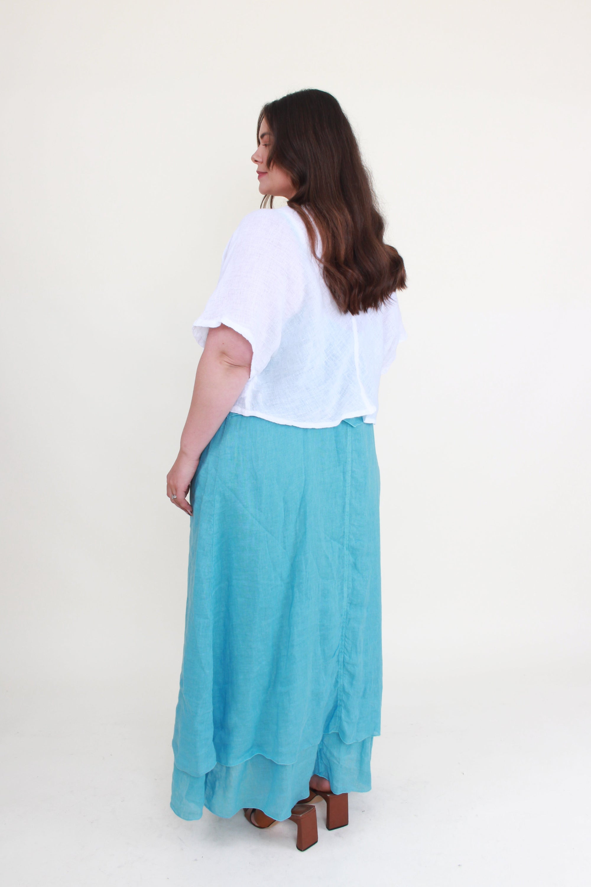 Woman wearing a white top and turquoise skirt on a white background back