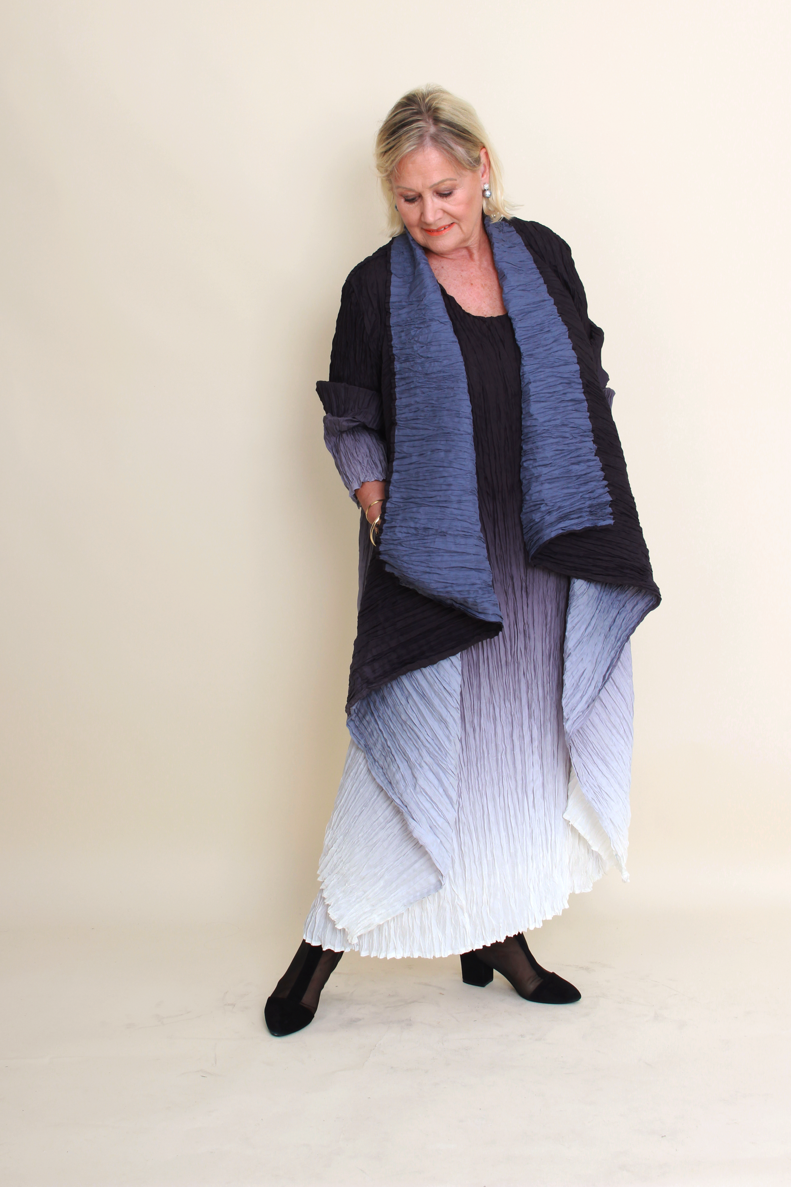 Woman wearing a long, dark blue and black textured scarf with a white dress against a beige background