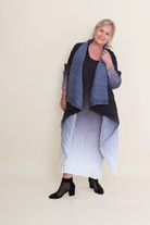 Woman wearing a long, dark blue and gray shawl over a black top and white skirt on a beige background