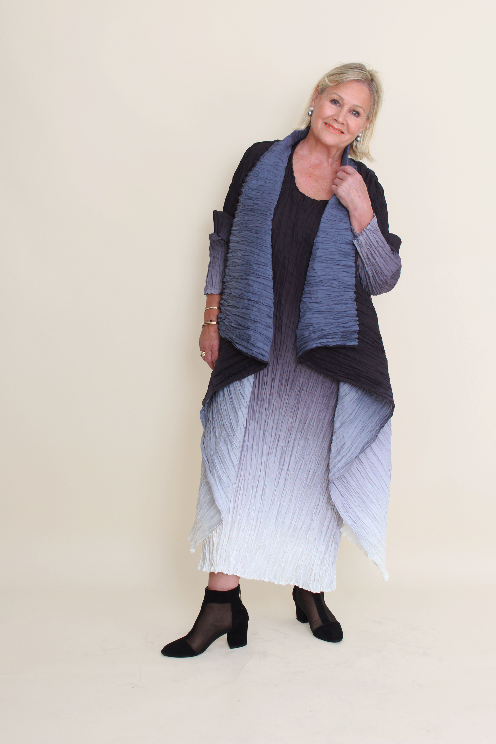 Woman wearing a long, dark blue and gray shawl over a black top and white skirt on a beige background