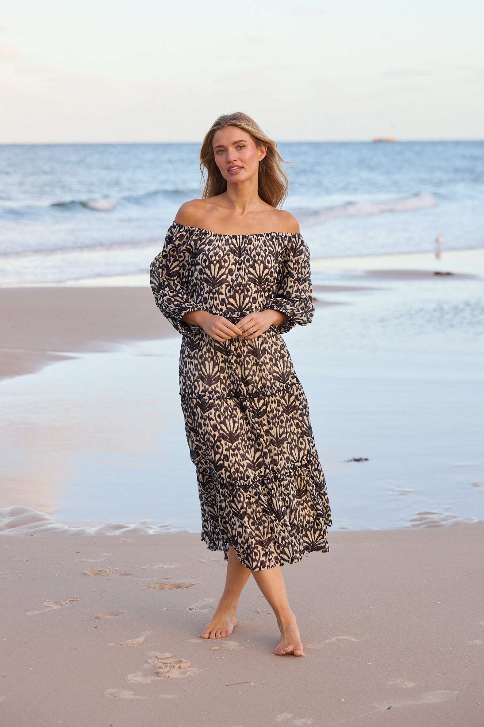 Woman in a floral dress standing on a beach with ocean waves in the background