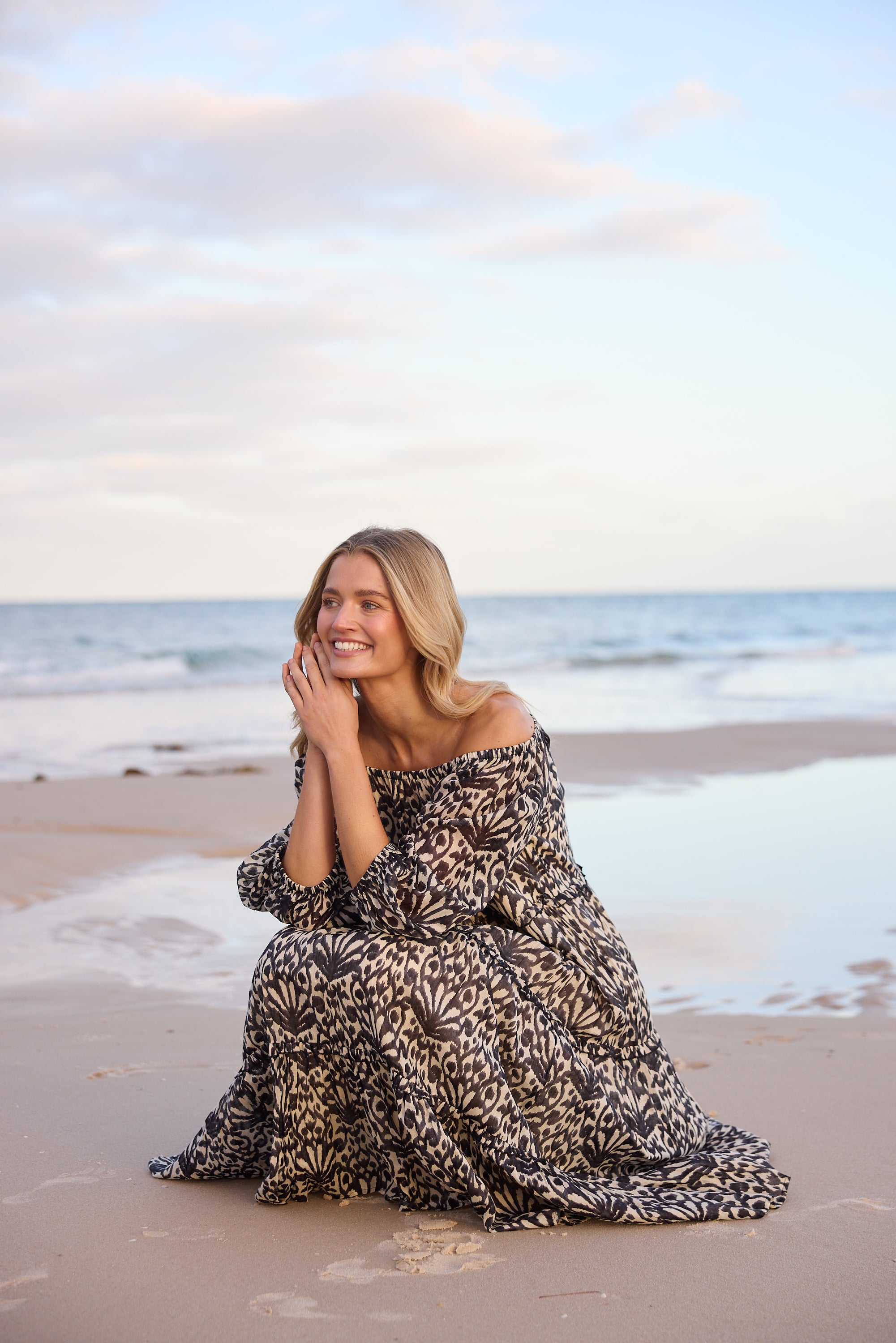 Woman in a patterned dress sitting on a beach with ocean waves in the background