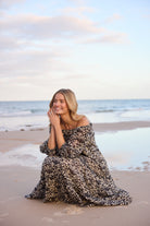 Woman in a patterned dress sitting on a beach with ocean waves in the background