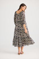 model wearing black cream long floral dress against white background back