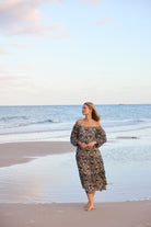 Woman in a floral dress standing on a beach with ocean and sky in the background