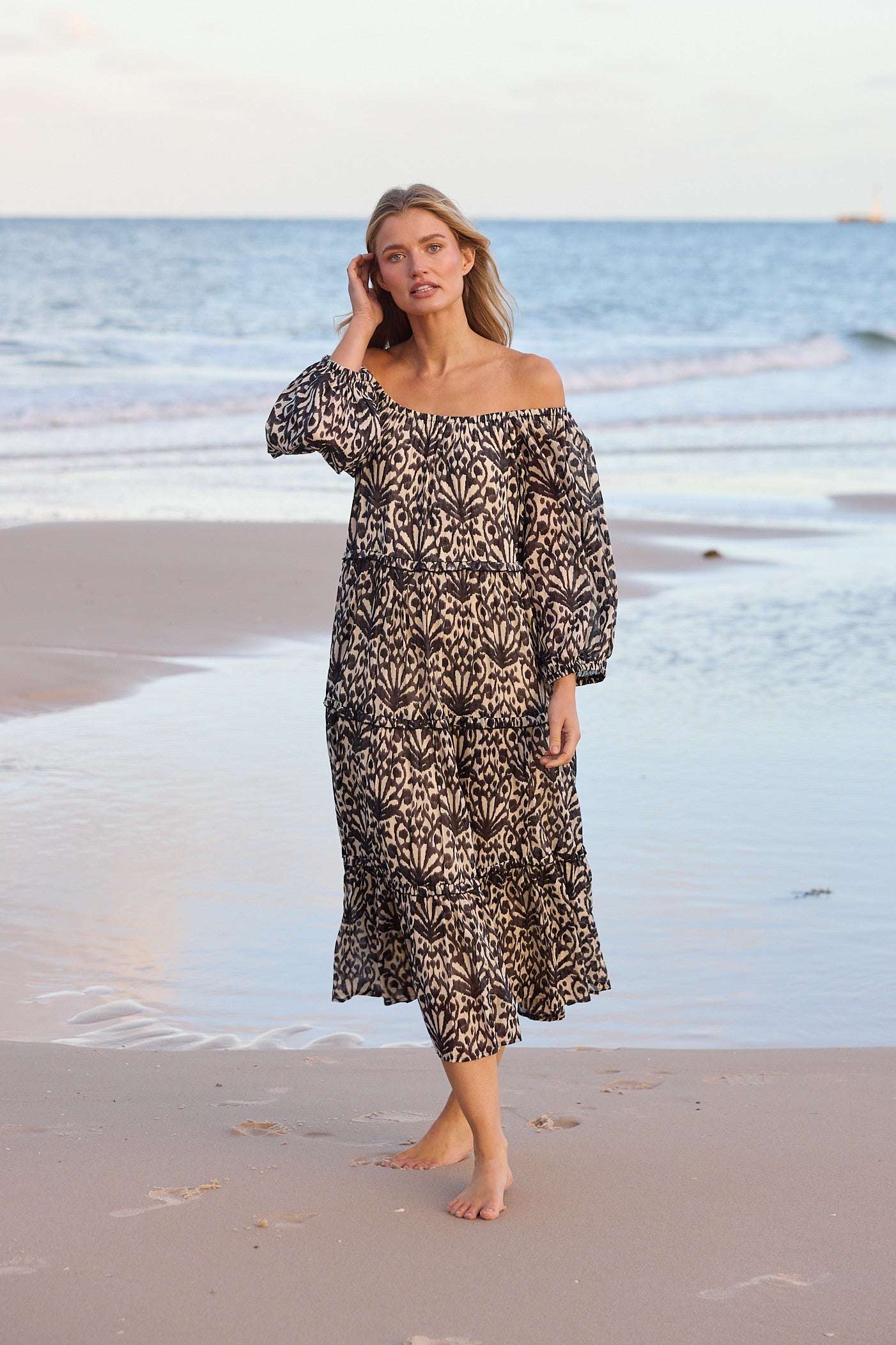 Woman in a patterned dress standing on a beach with ocean waves in the background