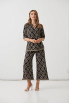 A woman modeling a matching two-piece set featuring a black and beige geometric pattern, consisting of a short-sleeve collared top and wide-leg cropped pants, set against a plain white studio background.