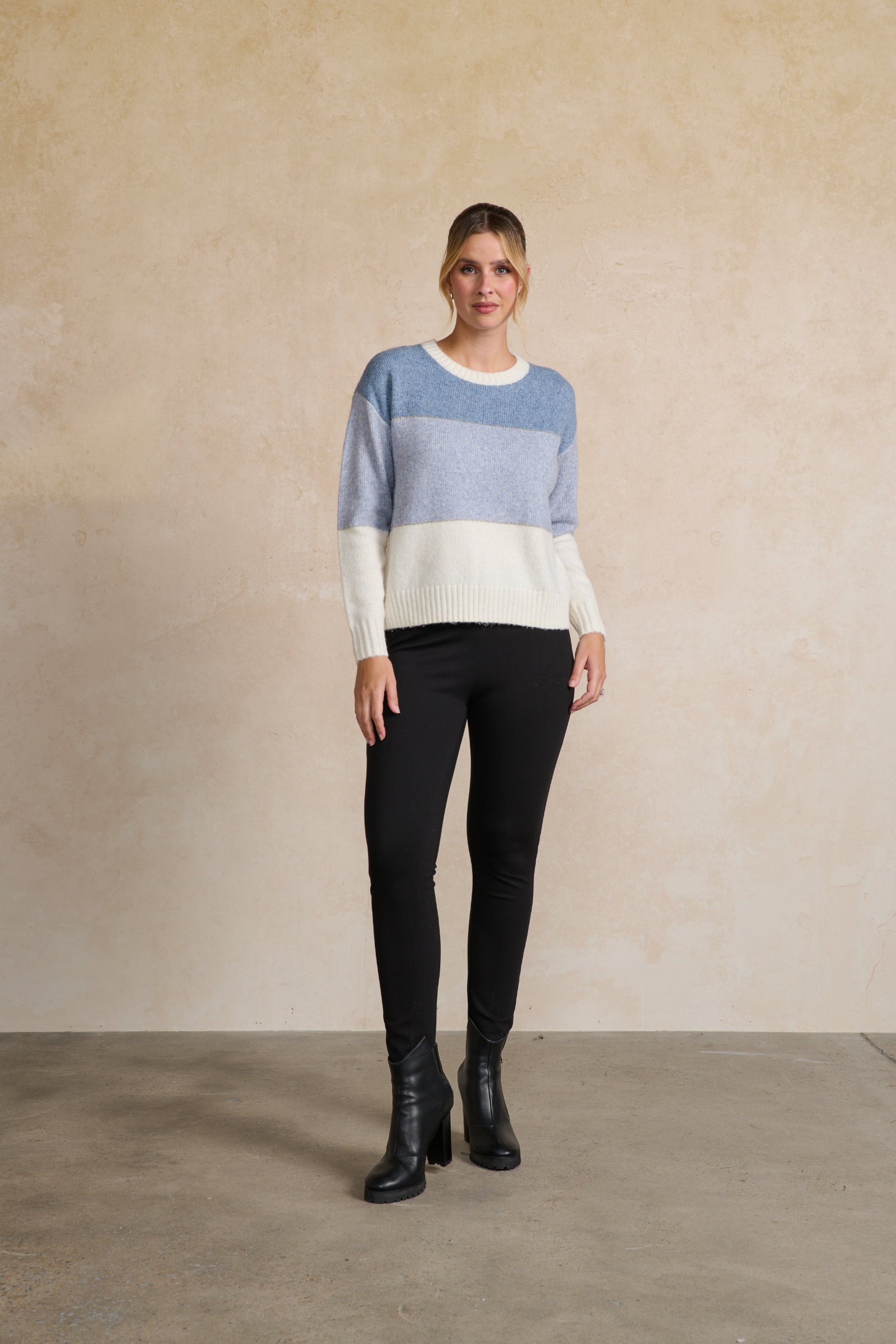 Woman wearing a striped sweater and black pants against a beige wall.