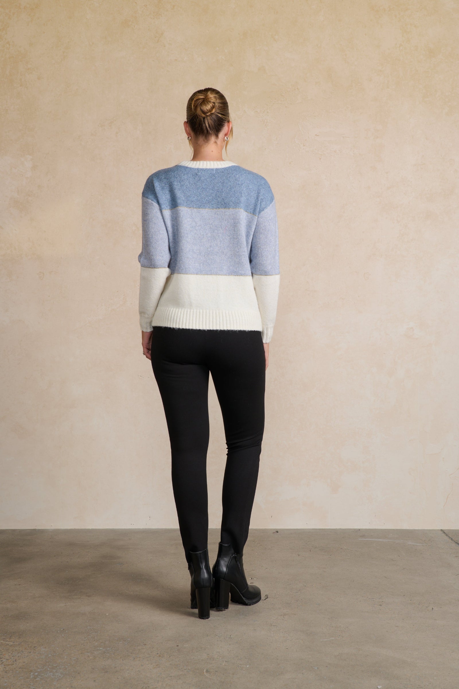 Person wearing a striped sweater and black pants against a beige wall.