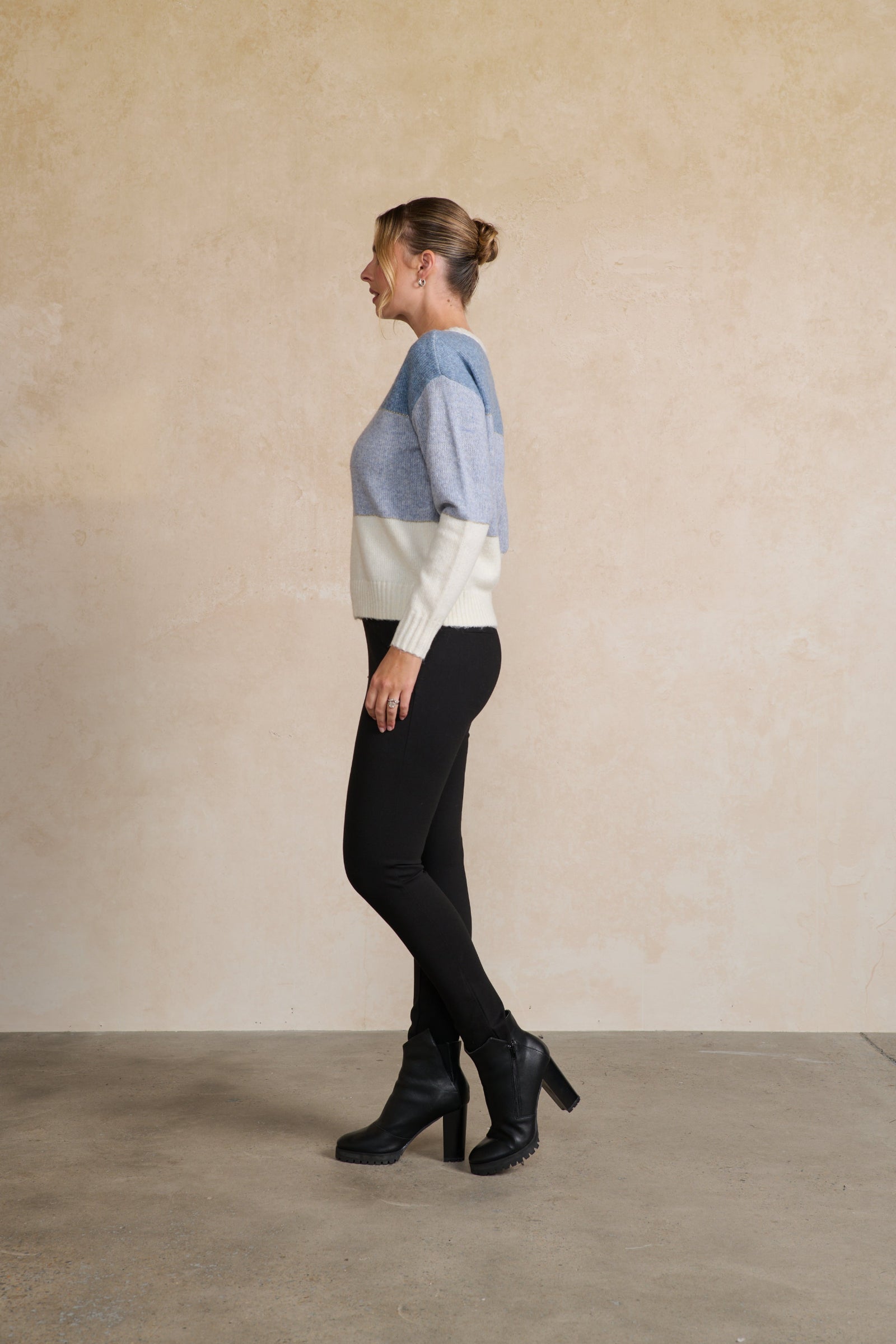 Person wearing a color-blocked sweater and black pants against a beige wall.