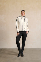 Person wearing a white jacket with black accents and black pants against a beige background