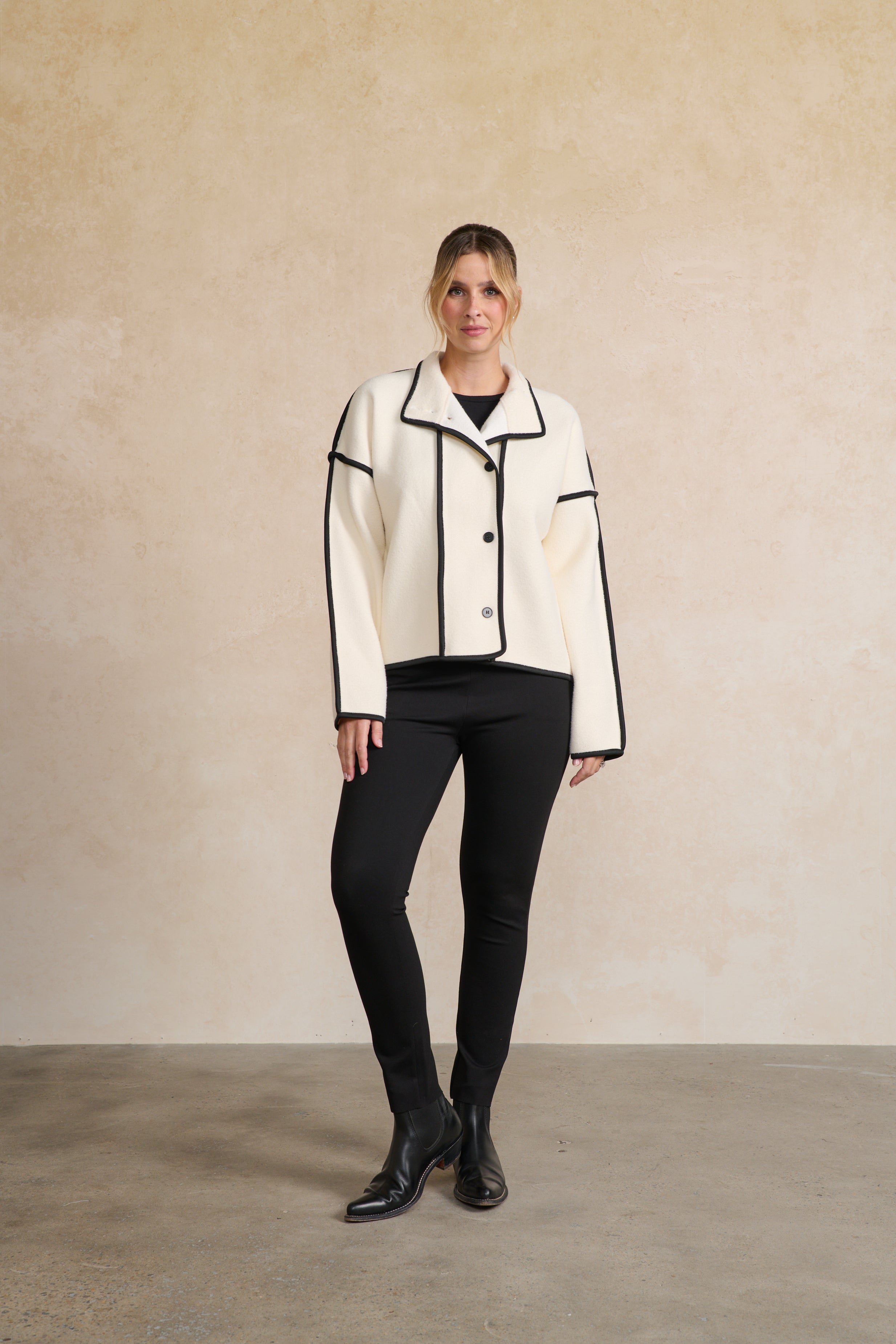 Woman wearing a white jacket with black accents against a beige background