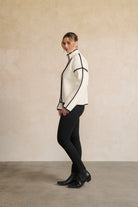 Woman wearing a white jacket with black trim against a beige wall side angle