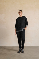 Person wearing a black textured sweater and pants against a beige wall.