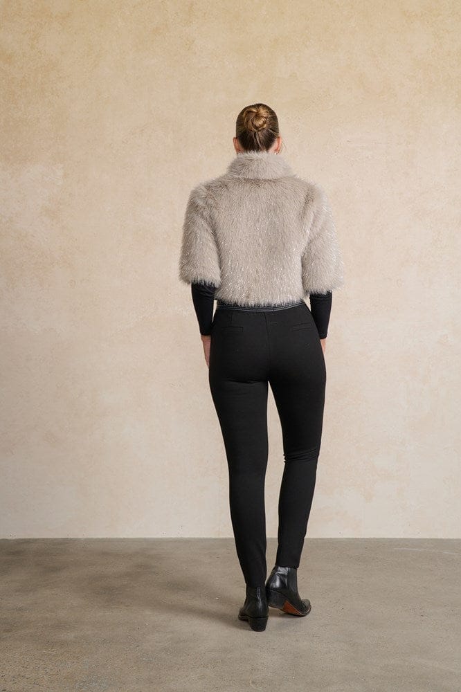 Person wearing a textured gray jacket and black pants against a beige wall back angle