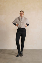 Person wearing a gray fur vest over a black outfit against a beige wall.