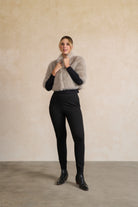 Person wearing a fluffy light gray sweater and black pants against a beige wall.