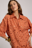 Woman wearing an orange lace shirt against a plain background