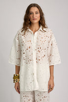 Woman wearing a white floral patterned shirt and pants on a gray background