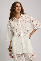 Woman wearing a white patterned shirt and pants on a gray background