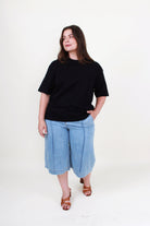 Woman wearing a black t-shirt and blue denim shorts on a white background