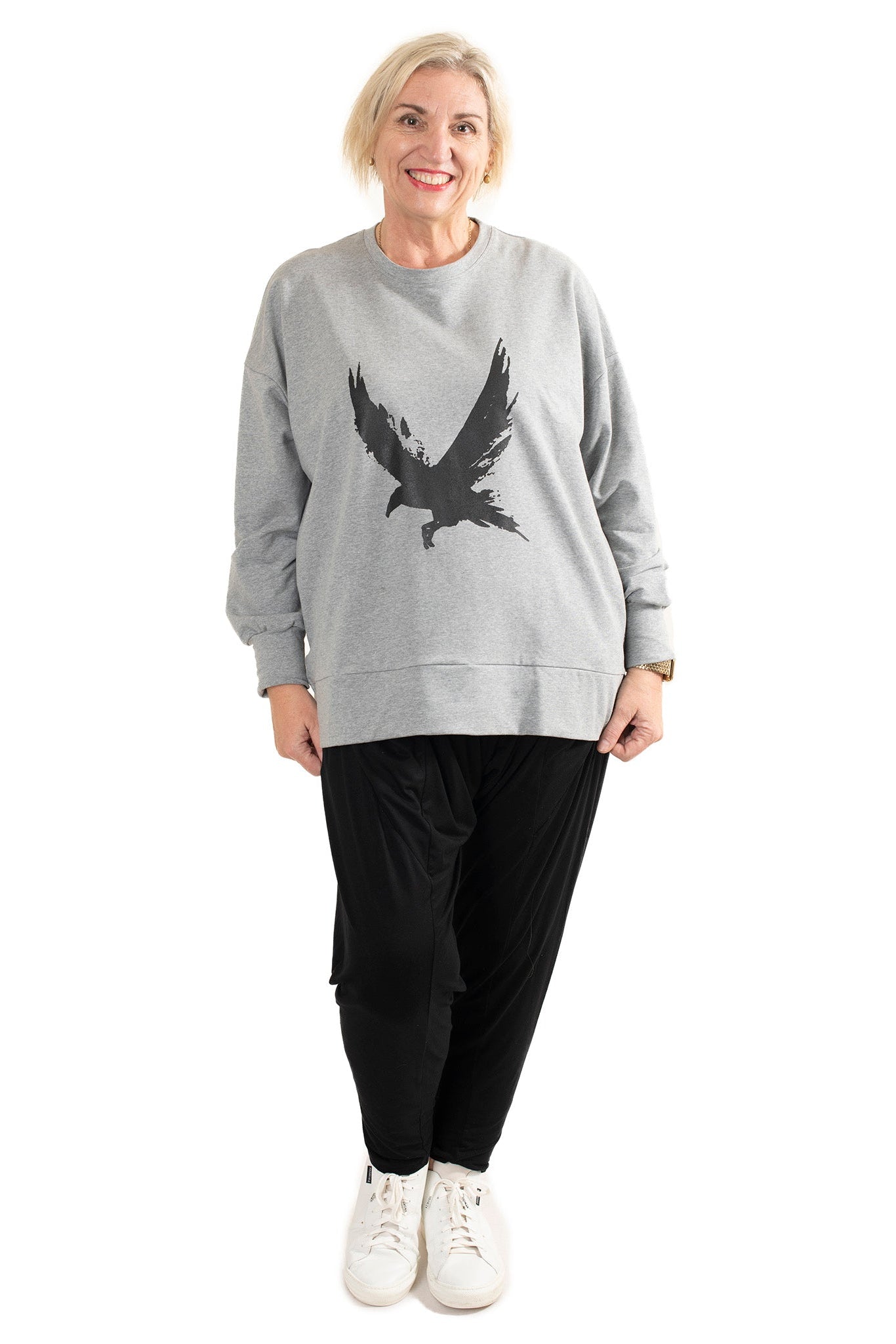 Person wearing a gray sweatshirt with an eagle design and black pants on a white background