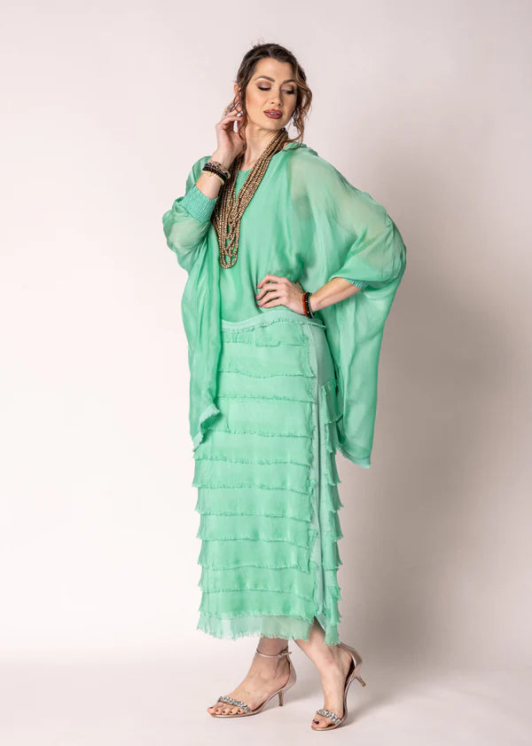 Woman wearing a light green dress with a matching shawl against a plain background