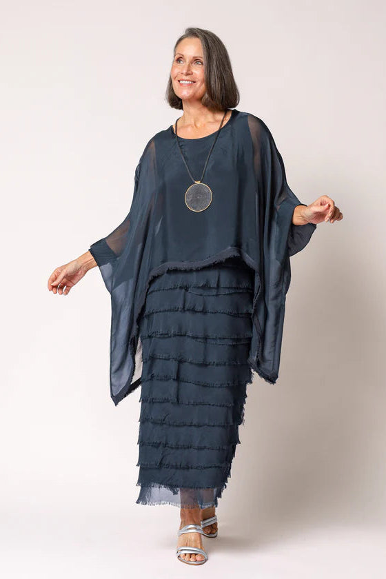 Woman wearing a dark blue layered outfit with a pendant necklace on a white background