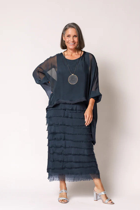 Woman wearing a navy blue layered dress with sheer sleeves against a white background