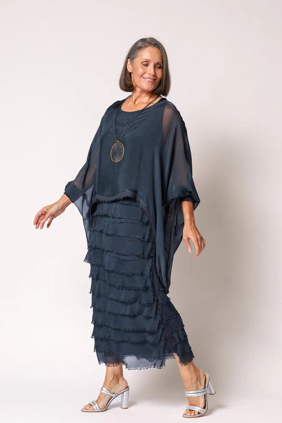 Woman wearing a dark blue layered dress with a plain background