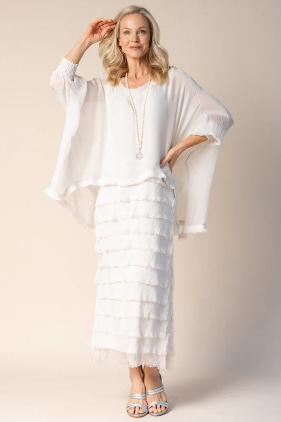 Woman wearing a white outfit with a sheer overlay against a plain background