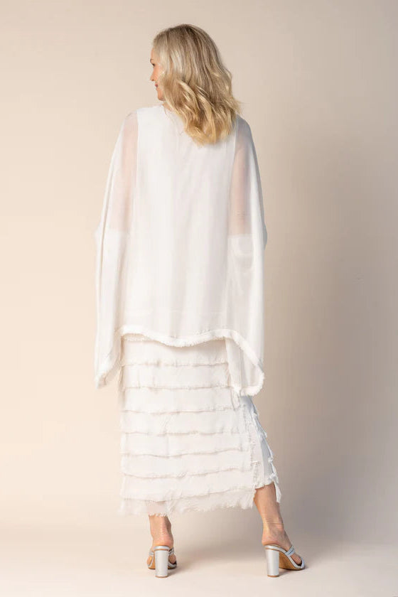 Woman wearing a white layered dress with a sheer overlay against a plain background