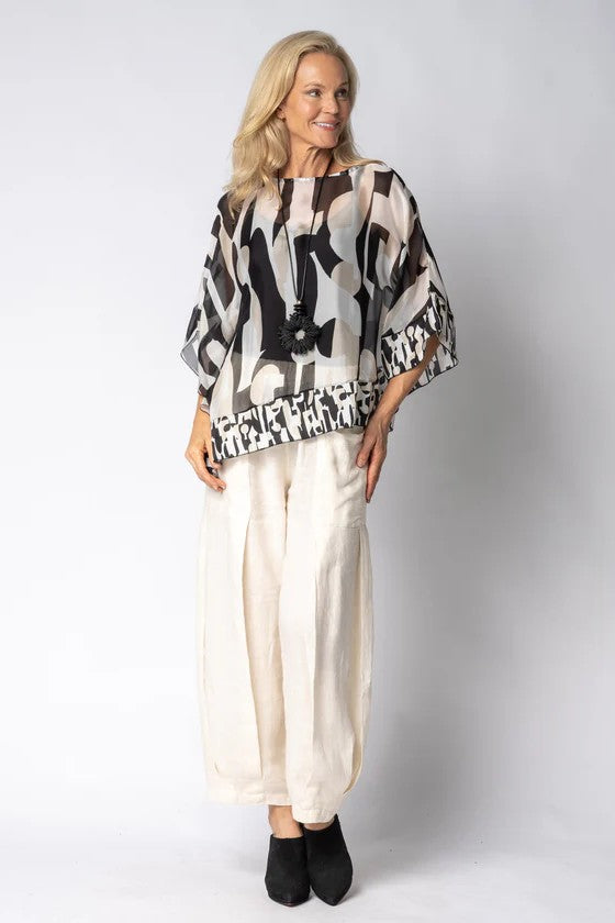 Woman wearing a patterned poncho and white pants on a plain background