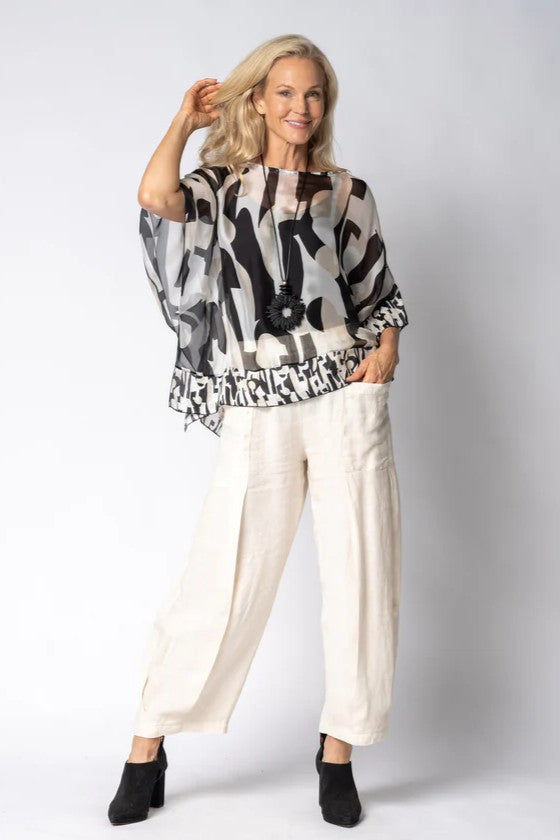 Woman wearing a patterned top and white pants against a plain background