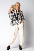 Woman wearing a patterned top and white pants against a plain background