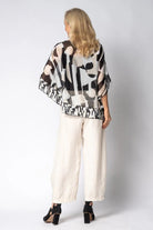 Woman wearing a patterned top and white pants against a plain background back angle