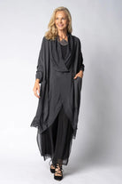 Woman wearing longline dark grey top over black dress on light grey background