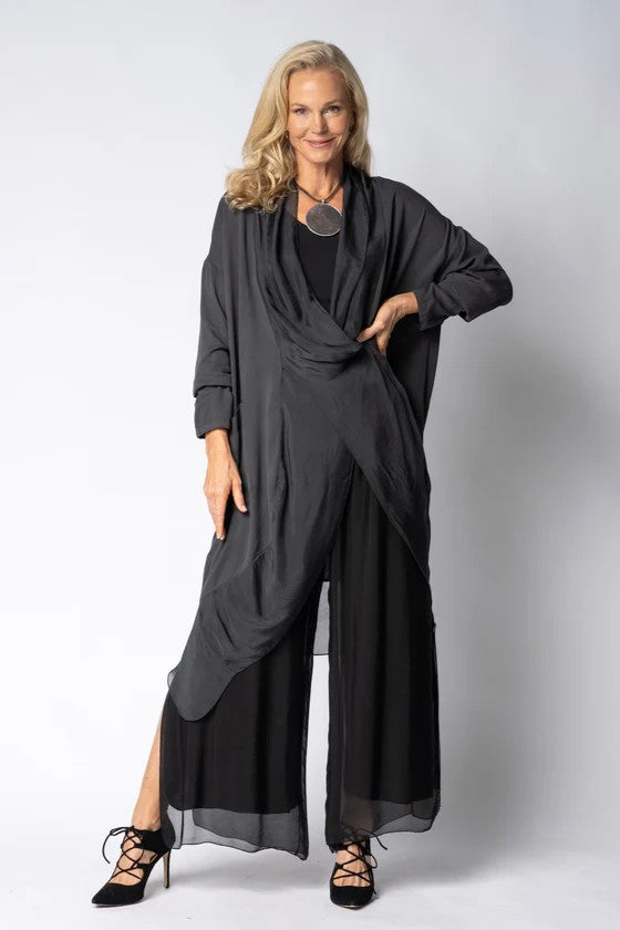 Woman wearing longline dark grey top over black dress on light grey background