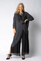 Woman wearing longline dark grey top over black dress on light grey background