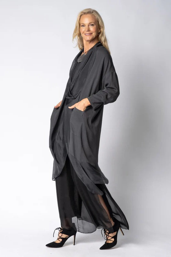 Woman wearing longline dark grey top over black dress on light grey background side angle