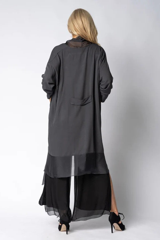 Woman wearing longline dark grey top over black dress on light grey background back angle