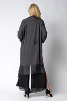 Woman wearing longline dark grey top over black dress on light grey background back angle