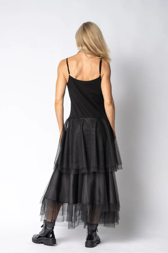 Woman wearing a black dress with sheer layers on a white background back angle