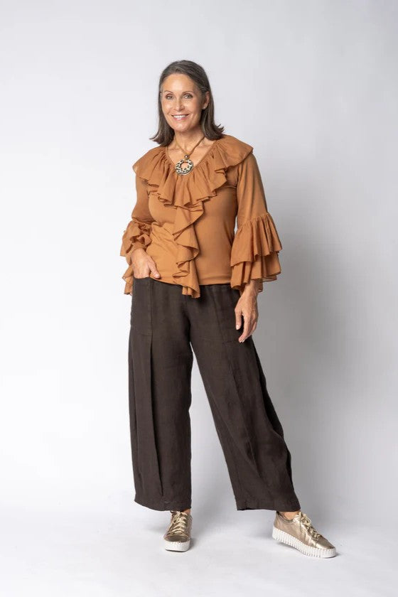 Woman wearing a brown ruffled blouse and dark pants on a white background