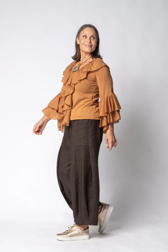 Woman wearing a brown ruffled blouse and dark pants on a white background